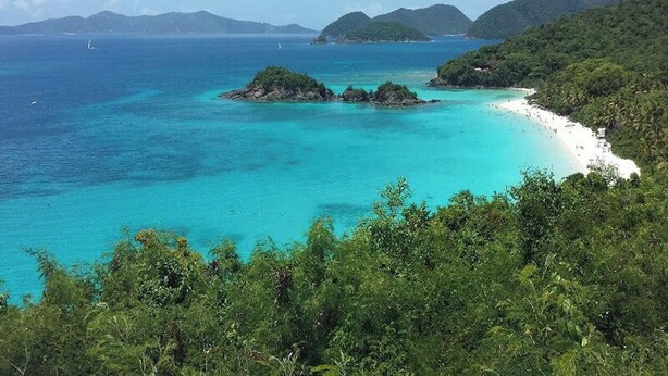 A coastal landscape with turquoise waters, a sandy beach, and lush greenery.