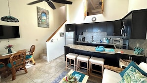 A compact kitchen with a central island, wooden dining set, and a ceiling fan.