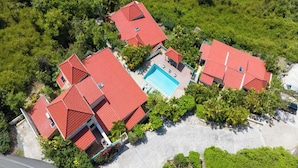An aerial view of a residential area with multiple houses, a swimming pool, and lush greenery.