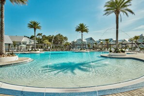 Une grande piscine extérieure entourée de palmiers et de chaises longues, sous un ciel d’un bleu éclatant.