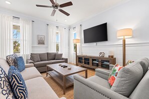 A living room with a sofa, armchair, coffee table, TV, and a ceiling fan.