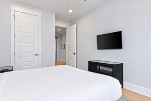 A bedroom with a bed, a TV mounted on the wall, and a door leading to another room.