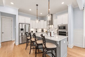 Una cocina moderna con armarios blancos, electrodomésticos de acero inoxidable y una isla central con taburetes de bar.