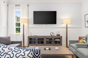 Una sala de estar moderna con un televisor de pantalla plana, dos lámparas, una mesa de centro de madera y un sofá gris.