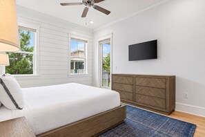 A bedroom with a bed, a ceiling fan, a TV, and a view of the outside.