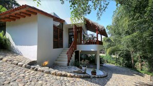 A house with a stone-paved entrance, a wooden staircase, and a thatched roof structure.