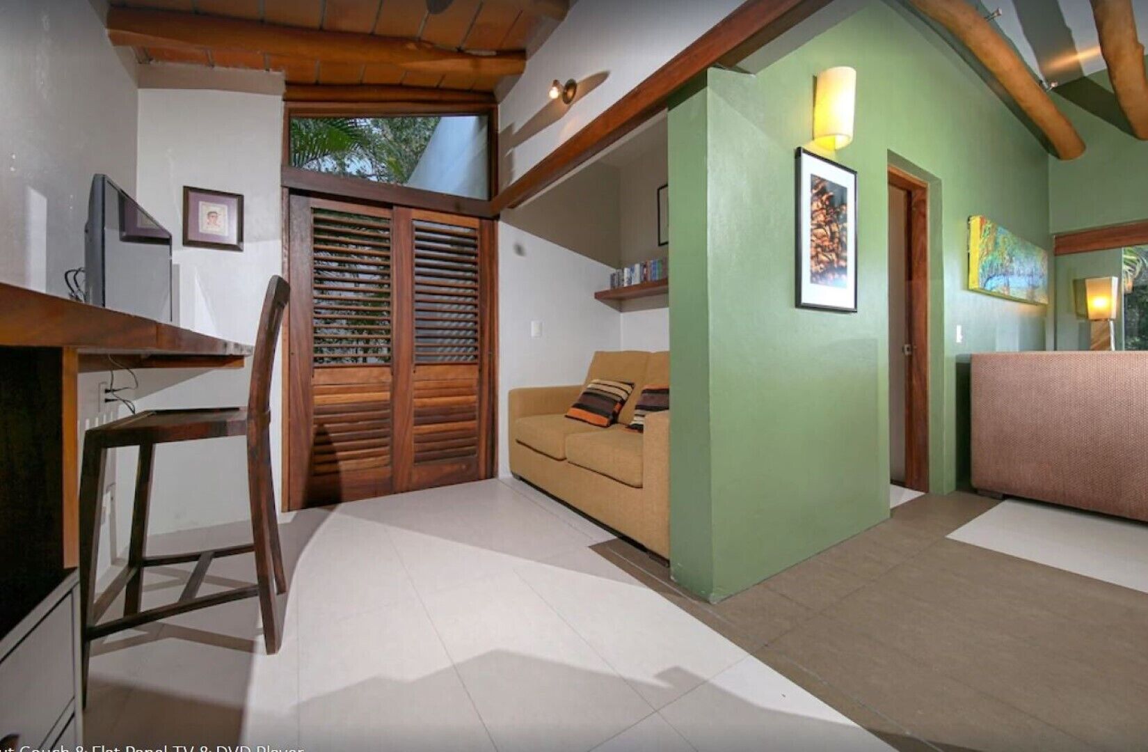 A room with a wooden desk, a sofa, a green accent wall, and a door with a picture frame.