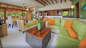 A modern living room with a green sofa, wooden coffee table, and a dining area with a table and chairs.