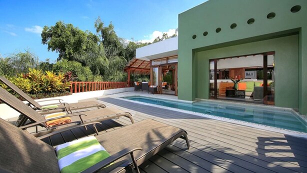 A pool area with lounge chairs, a pergola, and a modern building with large windows.