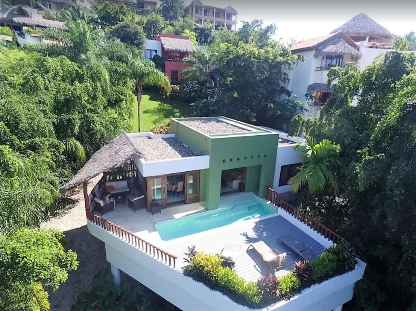 Une villa moderne dotée d’une piscine, entourée d’une végétation luxuriante et d’autres bâtiments.