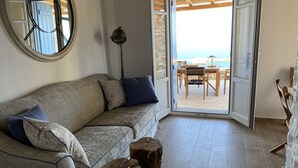 A cozy living room with a sofa, wooden stools, and a view of the beach through an open door. - Blue Calm Luxury Cycladic Villa in Sifnos island  (Αρτεμώνας Sifnos)