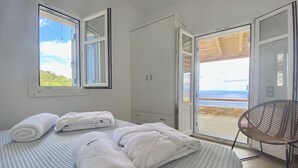A bedroom with a bed, a wardrobe, and a view of the sea through an open door. - Blue Calm Luxury Cycladic Villa in Sifnos island  (Αρτεμώνας Sifnos)
