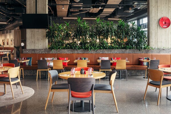 Un restaurante moderno con mesas redondas, sillas acolchadas y una gran pared vegetal.