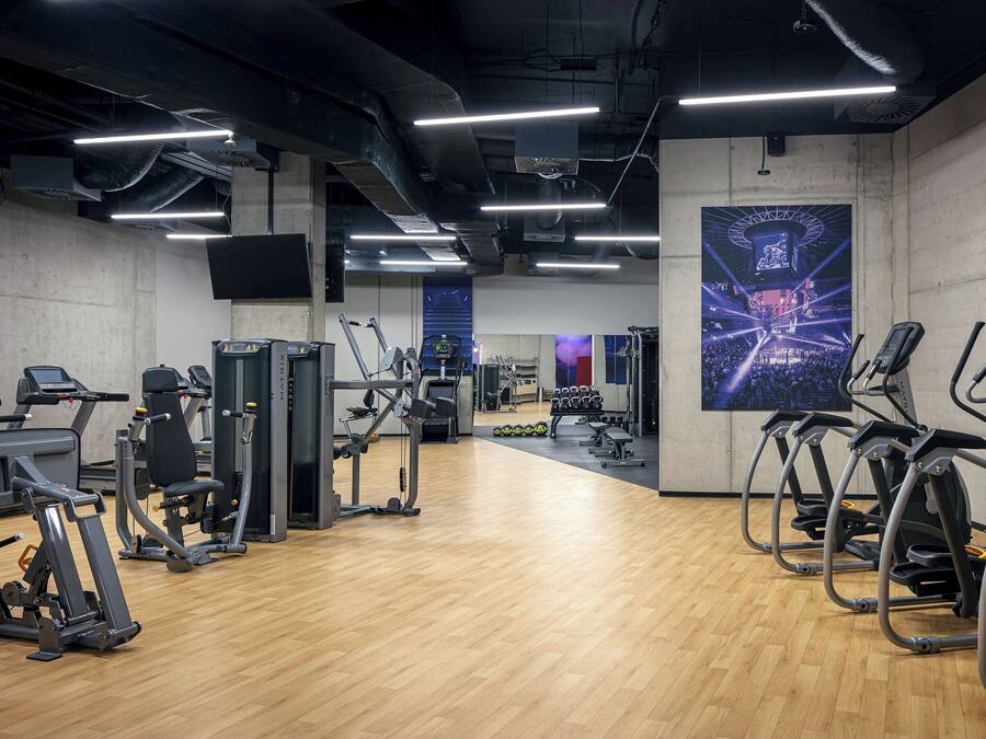 A gym with cardio machines, weight stations, and a large screen displaying an event.