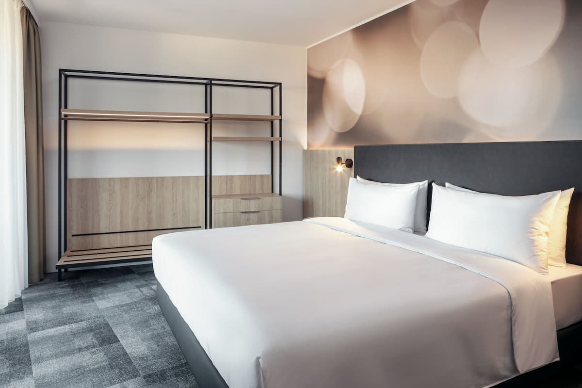Een moderne hotelkamer met een groot bed, een garderobe met verschillende vakken en een wandlamp.