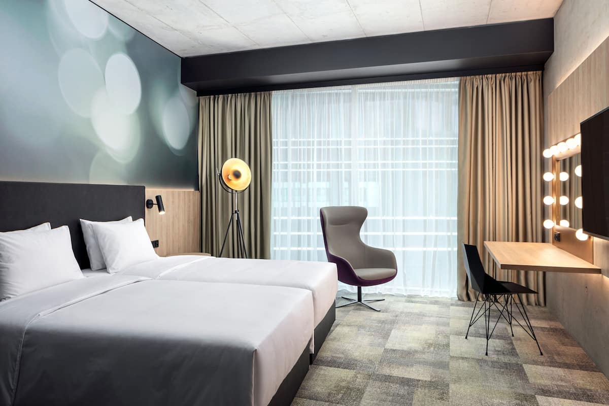 Een hotelkamer met twee bedden, een bureau met spiegel, een stoel en een vloerlamp.