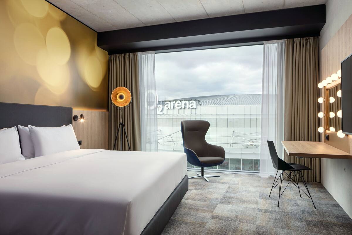 Een hotelkamer met een groot bed, een bureau met stoel, een spiegel met verlichting en uitzicht op buiten.
