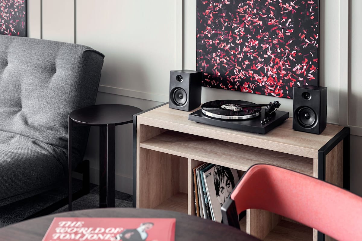 Een moderne woonkamer met een grijze bank, een klein zwart bijzettafeltje, een houten plank met boeken en een rode stoel.