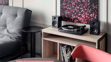 Una sala moderna con un sofá gris, una mesita auxiliar negra, un estante de madera con libros y una silla roja.