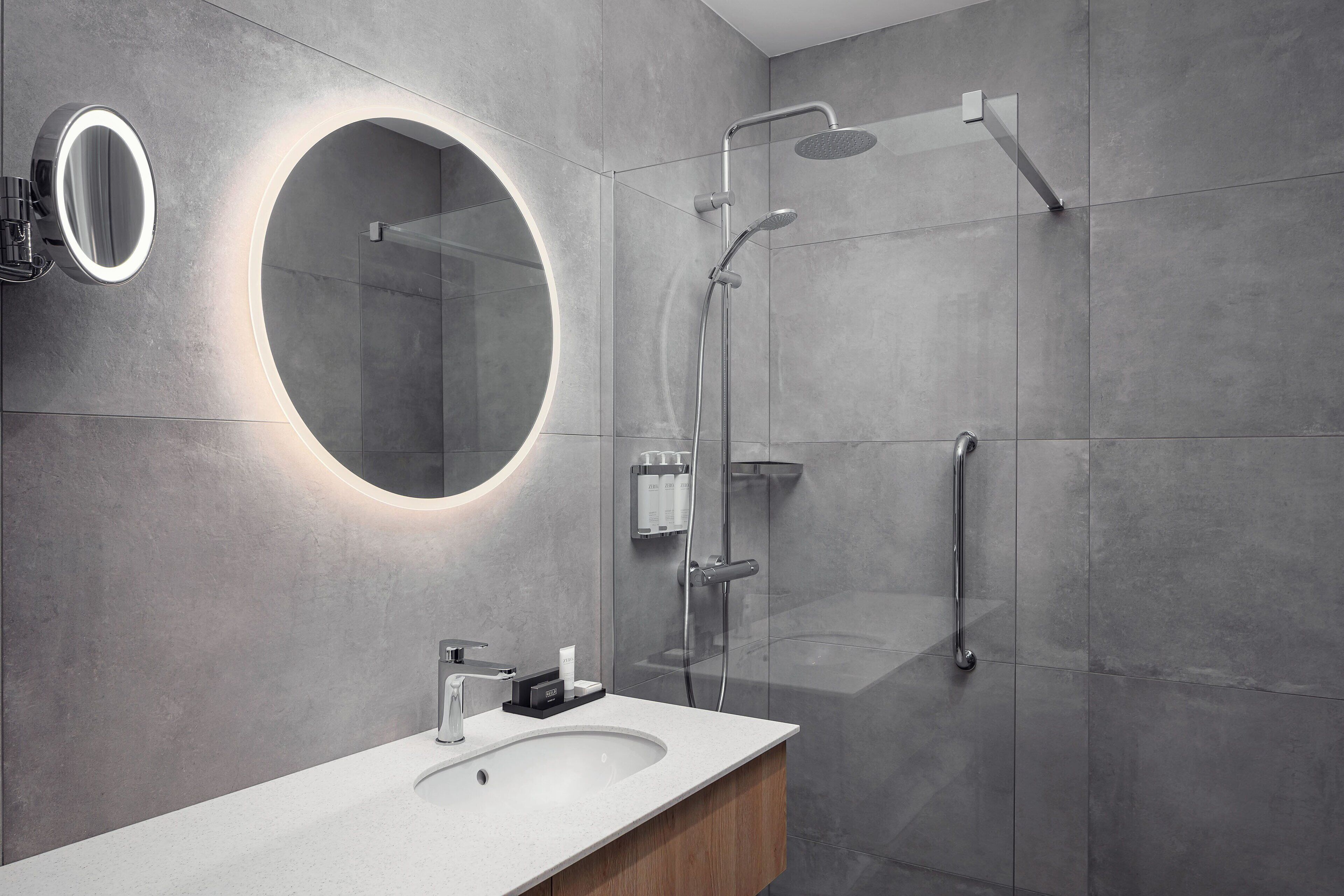 Un baño moderno con un espejo redondo, una ducha y un lavamanos.
