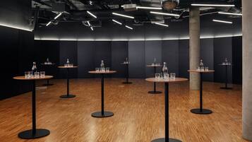 Ein modernes Interieur mit mehreren runden Tischen, auf jedem Tisch eine Flasche und Gläser, vor dunkler Wand und Holzboden.