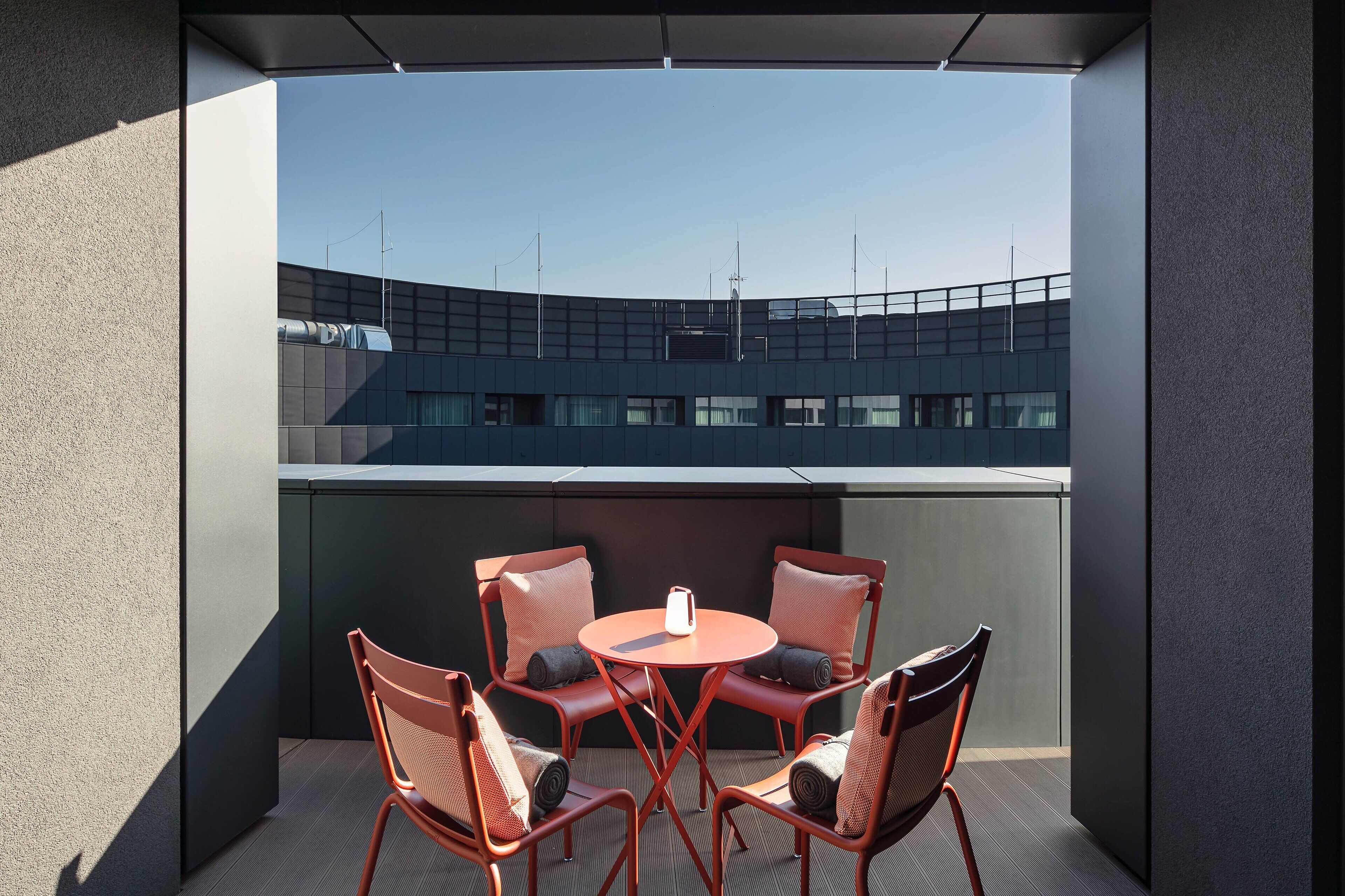 Un espace extérieur moderne aménagé avec une table ronde et quatre chaises, offrant une vue sur un bâtiment à la façade incurvée.