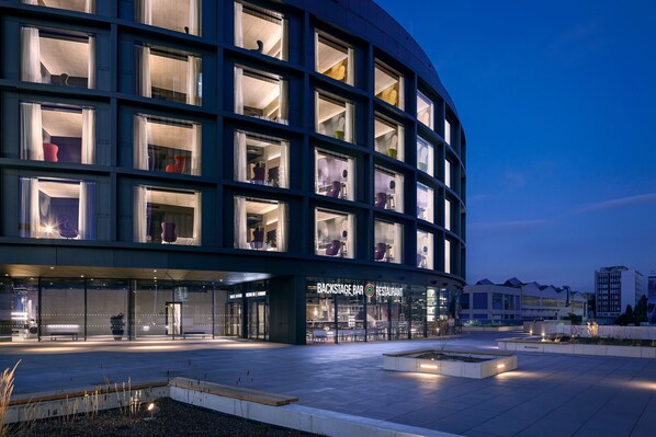 Un edificio moderno con fachada curva, ventanas amplias y un letrero que indica Backstage Bar Restaurant.