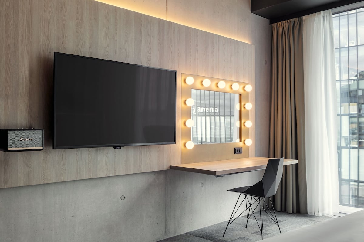 Een moderne kamer met een grote flatscreen televisie, een make-up tafel met verlichting, een houten bureau en een stoel.