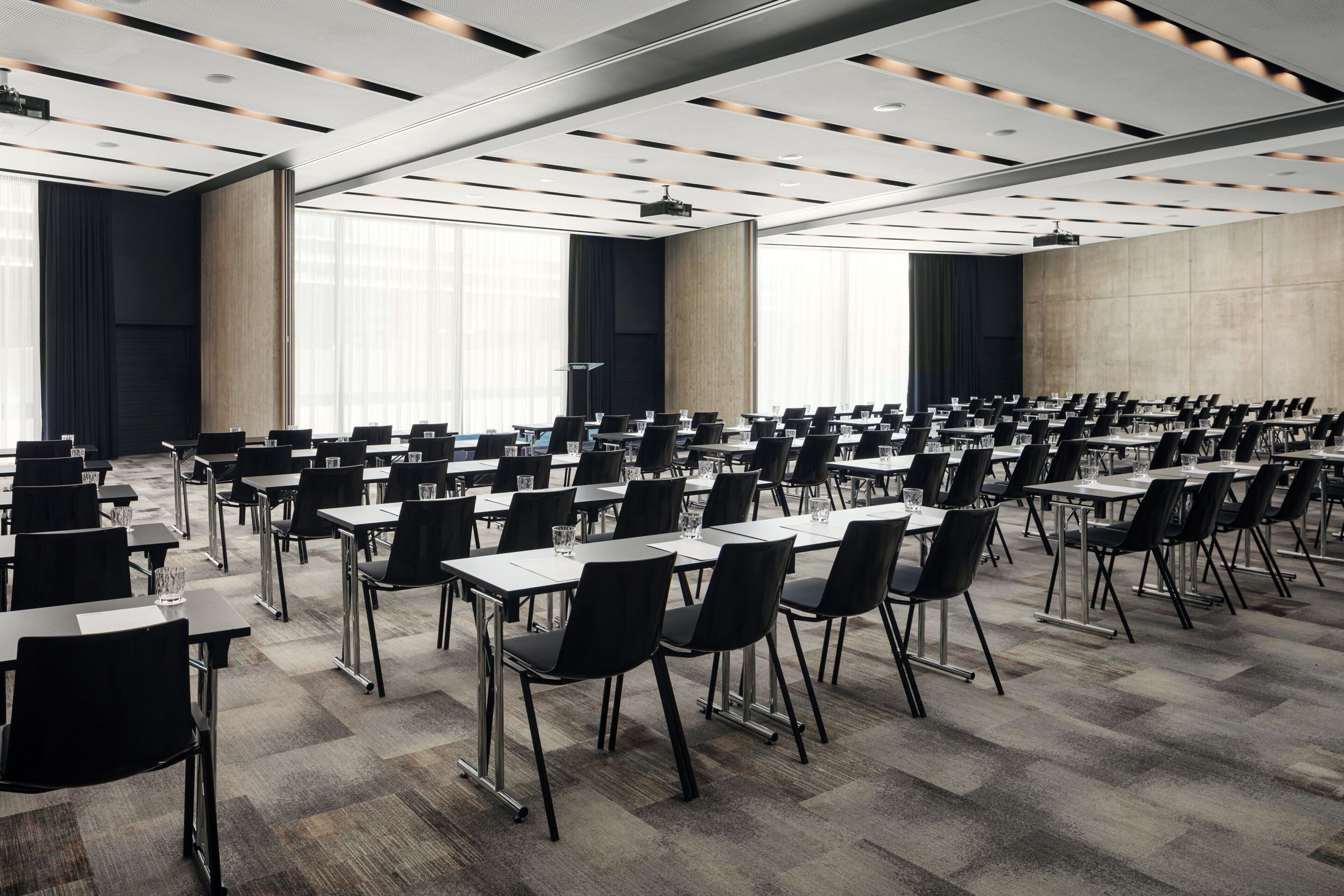 A conference room with rows of tables and chairs, large windows, and a modern ceiling design.