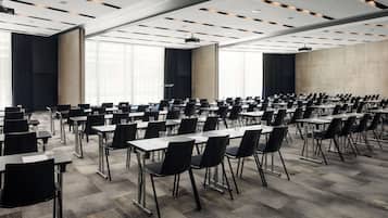 Un salón de conferencias con filas de mesas y sillas, amplias ventanas y un diseño moderno de techo.