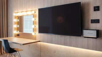 Una habitación moderna con una zona de tocador que incluye un espejo con iluminación, un televisor de pantalla plana y un altavoz Marshall.