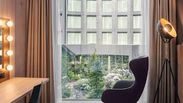 Une pièce dotée d’une grande fenêtre, d’un bureau avec une chaise, d’un lampadaire et d’un miroir avec éclairage intégré.