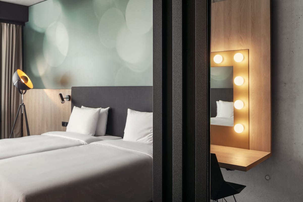 Een hotelkamer met een groot bed, een bedlamp, een spiegel met verlichting en een wand van hout.