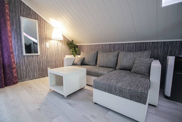 A modern loft bedroom with a sectional sofa, a white side table, and a large mirror.