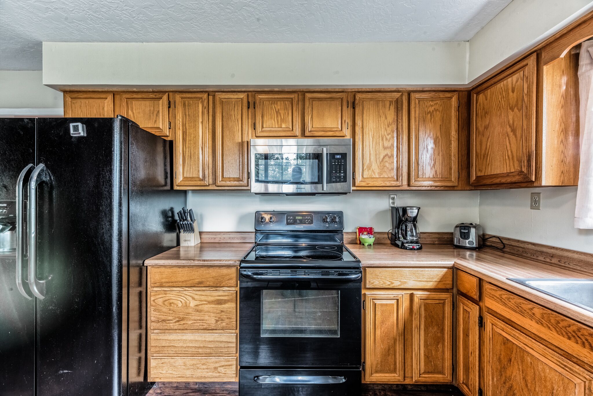 A kitchen with wooden cabinets, a black refrigerator, a stainless steel microwave, and a black stove.