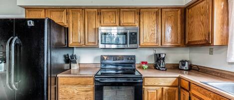 A kitchen with wooden cabinets, a black refrigerator, a stainless steel microwave, and a black stove.