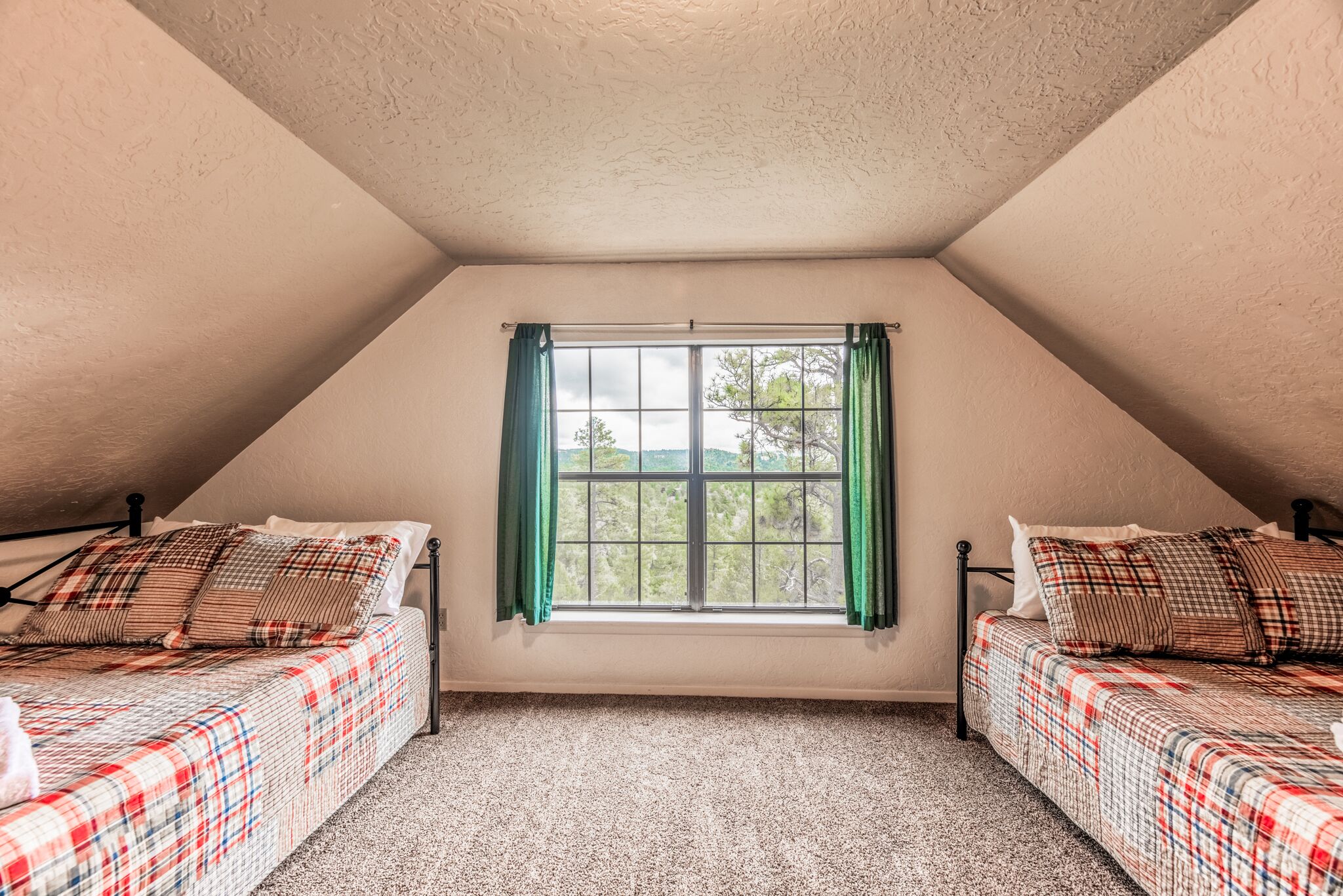 Une chambre avec deux lits, une fenêtre avec des rideaux et un plafond en pente.