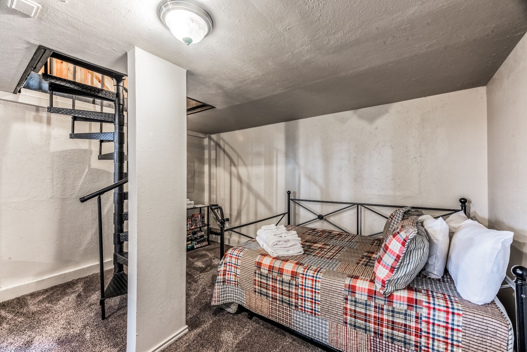 Une chambre à coucher avec un lit, une tête de lit en métal, une fenêtre et un escalier.