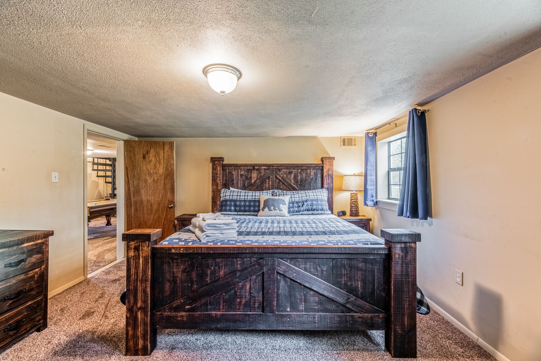 A bedroom with a wooden bed, a nightstand, a lamp, and a window with curtains.