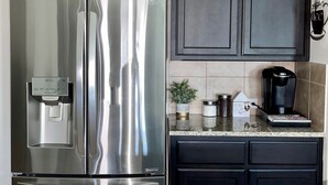 A stainless steel refrigerator with a water dispenser, dark cabinetry, and a coffee maker on the countertop.