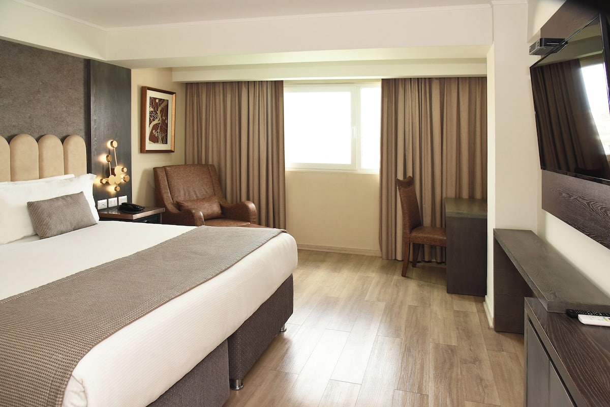 A hotel room with a large bed, a chair, a desk, and a TV.