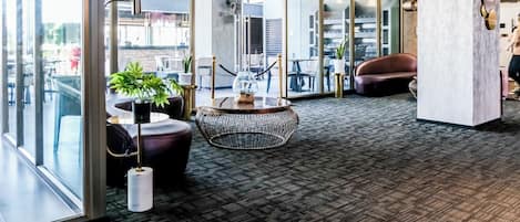 A modern interior with glass walls, a patterned carpet, a round table with a plant, and a leather chair.