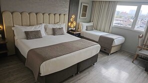 A hotel room with a large bed, a smaller bed, a desk with a lamp, and a view of the city through the window. - Hotel HW Libertad (Santiago)