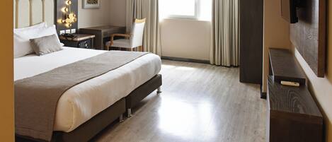 A hotel room with a large bed, a desk, a chair, a TV, and a window with curtains.