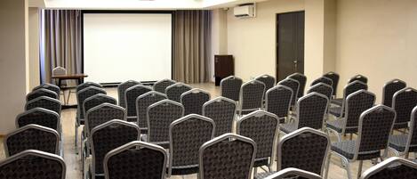 Una sala de conferencias con hileras de sillas, una pantalla de proyector y un equipo de aire acondicionado.