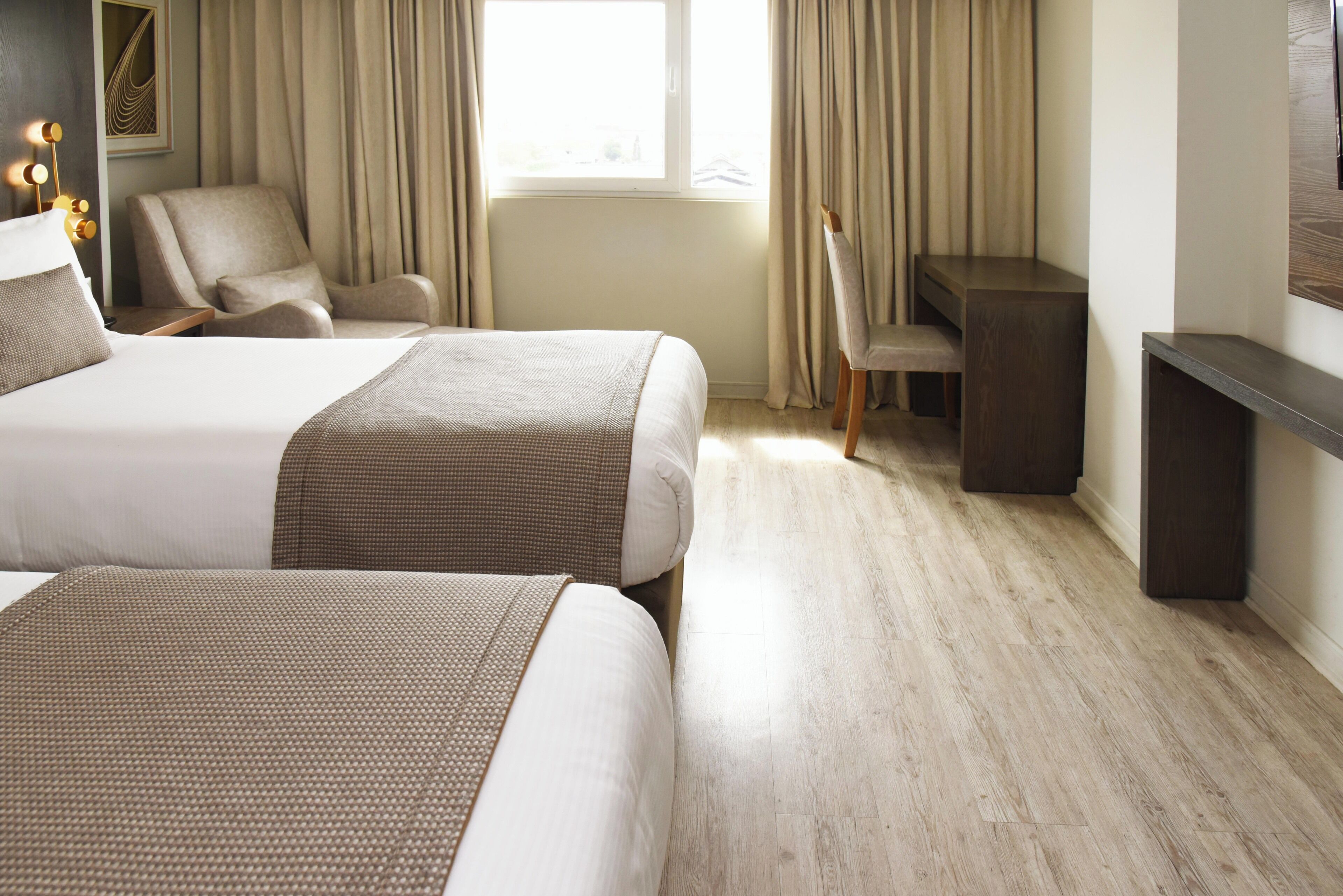 Habitación de hotel con dos camas, un escritorio, una silla y un ventanal con cortinas.
