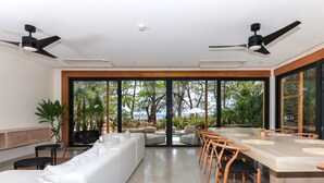 A modern dining area with a long table, white sofa, and ceiling fans. -  Luxury Beachfront Villa with private pool at Nantipa (Cóbano)
