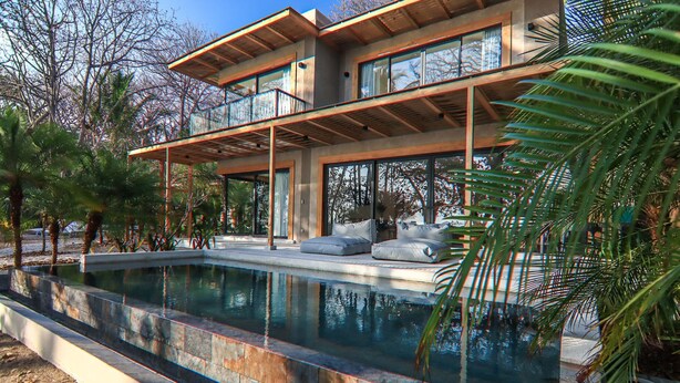 A modern two-story house with a swimming pool, outdoor seating, and a view of the surrounding trees. -  Luxury Beachfront Villa with private pool at Nantipa (Cóbano)