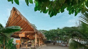 A thatched-roof building with a covered outdoor seating area, surrounded by tropical vegetation. -  Luxury Beachfront Villa with private pool at Nantipa (Cóbano)