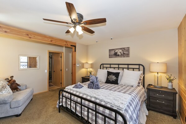 Une chambre à coucher comprenant un lit, des tables de chevet, un ventilateur de plafond, un miroir et une porte.